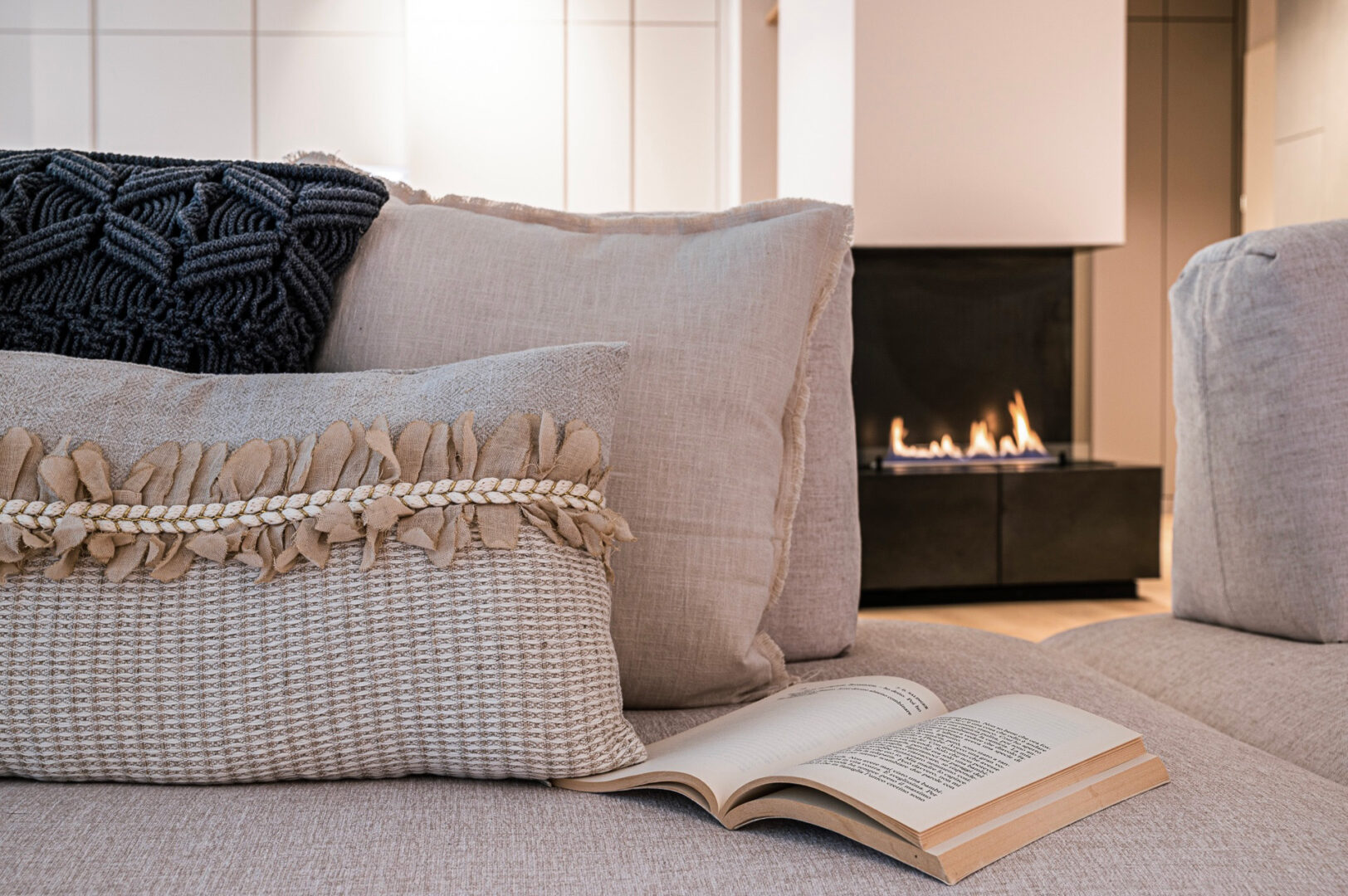 Kuschelige Stimmung mit Feuer im Kamin und Blick auf die Kissen auf dem Sofa, Buch