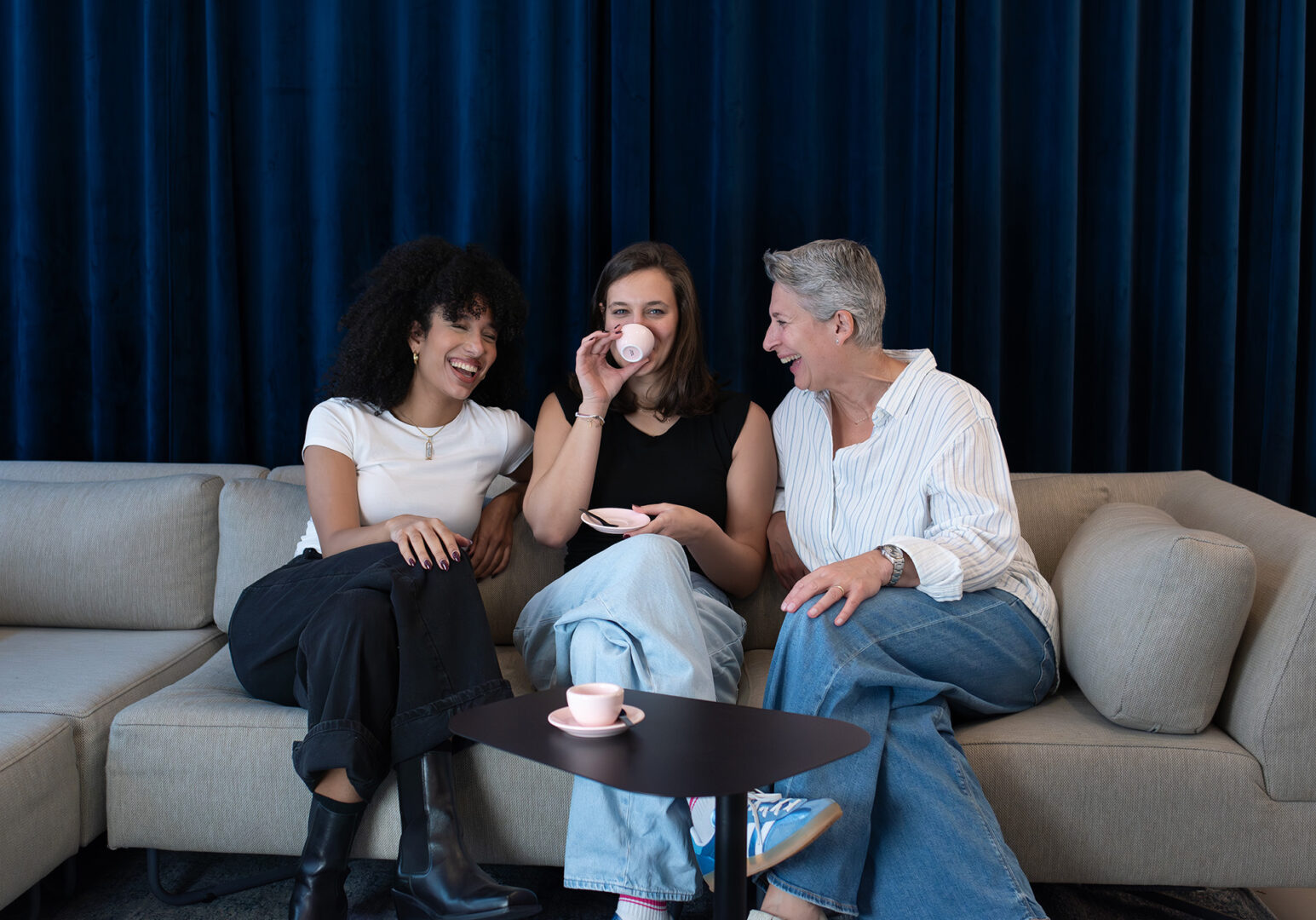 Herzliches Team, Kontakt zu fineconnect, Andrea Gartenmaier, Marianne Awad und Nicole Gartenmaier auf Sofa sitzend, freundlich lachend, Nicole Kaffeetasse in der Hand